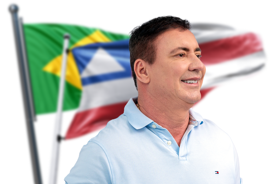 Ditinho sorrindo em frente às bandeiras do Brasil e da Bahia